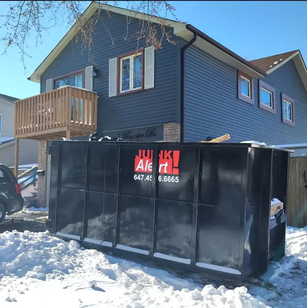 Bin on a snowy driveway beside a renovated house