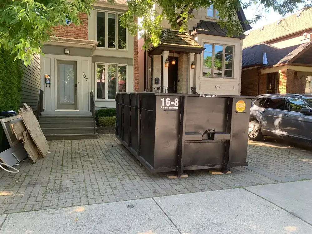 Sixteen yard bin placed on a driveway beside a house renovation